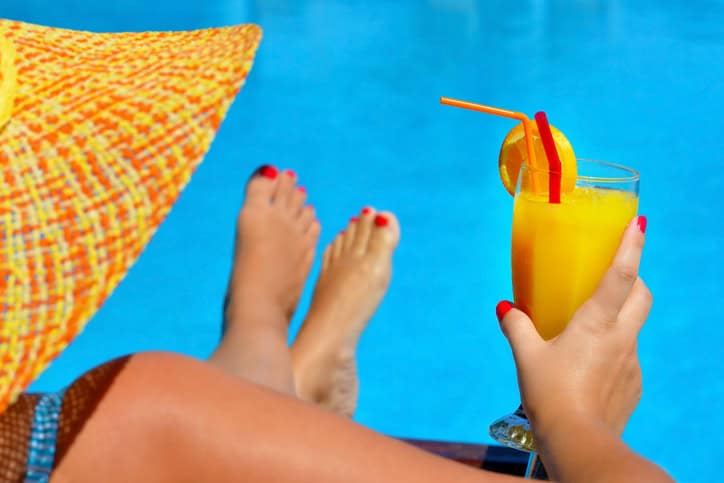 Woman relaxing by the pool with an orange juice cocktail and summer hat